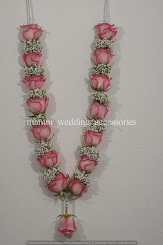 a pink rose flower necklace is hanging from a hook on a white wall with two candles