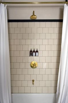 a bathroom with white tile and gold fixtures, shower curtain is open to reveal the bathtub