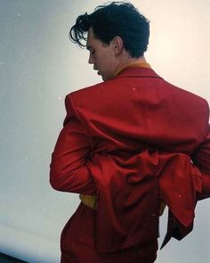 a man in a red suit with his back turned to the camera, standing against a white wall