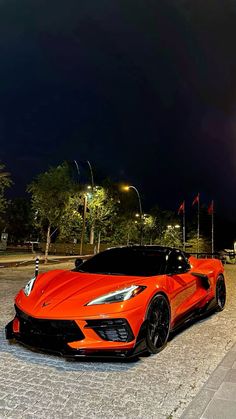 an orange sports car parked on the side of a road at night with street lights in the background