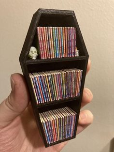 a hand holding a small book shelf with books on it's sides in front of a white wall