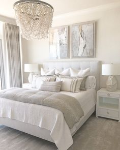 A bright bedroom with a large bed, two white nightstands with lamps, a crystal chandelier, and abstract art above the headboard. The decor is neutral with light tones. Modern White Bedroom, Neutral Bedroom Decor, White Room Decor, Classy Bedroom, White Bedroom Furniture, Redecorate Bedroom, Bedroom Refresh, Room Makeover Bedroom