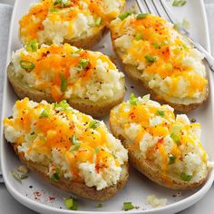 baked potatoes topped with cheese and green onions on a white plate next to a fork