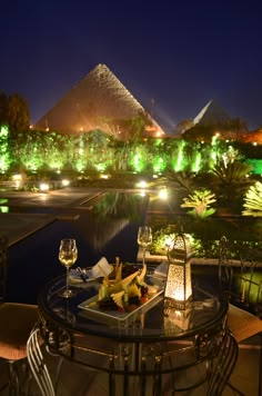 an outdoor table with food and wine on it in front of the pyramids at night