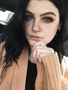 a woman with freckles and piercings on her nose sitting in a car