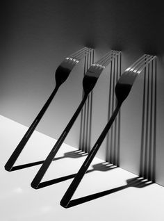 four forks are lined up in a row on a table with shadows from the wall behind them