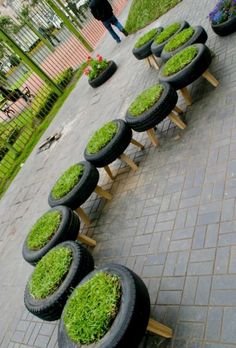 a row of tires with grass growing out of them sitting on top of a sidewalk