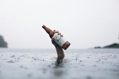 a person holding a beer bottle in the water with their hand out to touch it