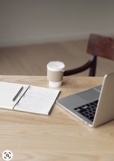 a laptop computer sitting on top of a wooden table next to a cup of coffee