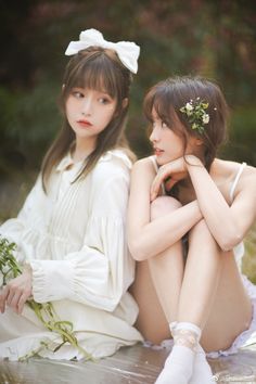 two young women sitting on the ground next to each other with flowers in their hair