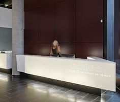 there is a woman sitting at the front desk in an office building with lights on