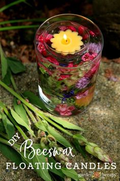 a candle that is floating in some water with flowers on the ground next to it