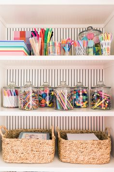 organized craft supplies in glass jars on shelves with striped wall paper and straw baskets below