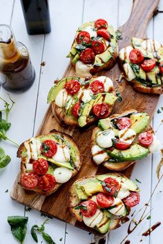 several open faced sandwiches with tomatoes, avocado and cheese on a wooden cutting board