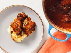 a white plate topped with meat next to a pot of stew