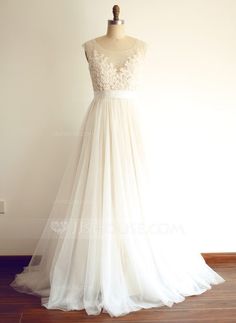 a white dress on a mannequin stand in front of a wall and wooden floor