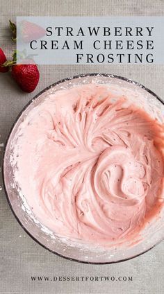 a bowl filled with pink frosting next to two strawberries