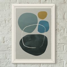 a framed art print on a brick wall with a white frame and blue, yellow and green circles