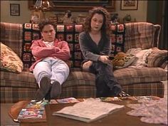 two women sitting on a couch in front of a coffee table with magazines and papers