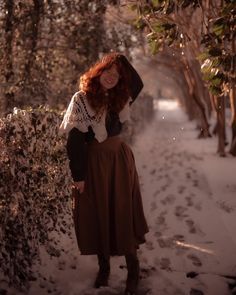 Red haired girl wearing a green waffle knit sweater tucked into a brown wool skirt with a “v” waist detail. She has on a crochet cream color shawl for added layering. She’s standing on a snowy pathway next to a hedge covered in snow. There are snowflakes catching the light beams. She’s smiling and holding her hair from being blown into her face by the wind. Cottagecore Outfits For Winter, Cottagecore Winter Dress, Cottagecore Rainy Day Outfit, Anne Shirley Outfit, Winter Outfits Cottagecore, Cottagecore Christmas Outfit, Little Women Inspired Outfit, Cottagecore Aesthetic Outfits Winter, Cottage Witch Outfit