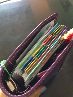 a person is holding a purple wallet full of pens and pencils