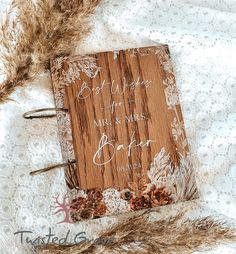 a wooden notebook with writing on it sitting on a white lace covered tablecloth next to dried feathers