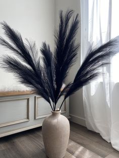 a vase with some black feathers in it on the floor next to a white wall