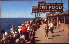 people are walking on the pier by the water while others watch from the dock area