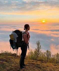 a woman standing on top of a hill with a backpack in front of the clouds