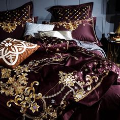 a bed covered in purple and gold comforter with decorative pillows on top of it