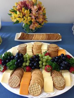 a platter of cheese, crackers and grapes on a blue table cloth