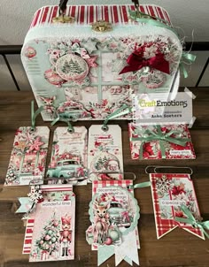 an assortment of christmas cards and tags on a wooden table next to a suitcase with ribbon