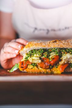 a close up of a person holding a sandwich on a plate with tomatoes and broccoli