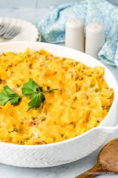 a casserole dish with cheese and vegetables in it on a white plate next to a wooden spoon