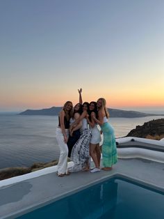 four women are posing for a photo by the pool at sunset with their arms in the air