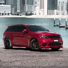 a red jeep parked in front of a body of water with buildings in the background