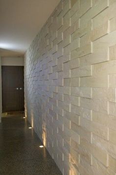 an empty hallway with white brick walls and lights on either side of the wall, leading to another room