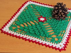 a crocheted placemat with a pine cone on top and a red white and green border