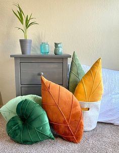 four decorative pillows sitting on the floor next to a nightstand with a potted plant