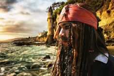 a man with dreadlocks and a red bandana standing in front of the ocean