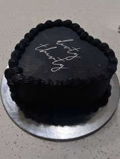 a black cake with writing on it sitting on top of a silver platter next to a knife