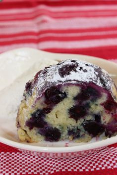 a blueberry muffin with powdered sugar on top sits in a white bowl