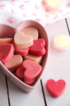 a heart shaped container filled with hearts next to candles