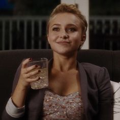 a woman sitting on a couch holding a glass in her hand and looking at the camera