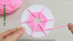 someone is knitting yarn on top of a piece of white paper with pink yarn next to it