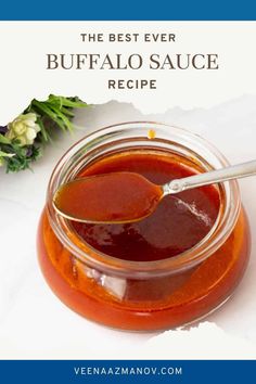 the best ever buffalo sauce recipe in a glass jar with a spoon and flowers behind it