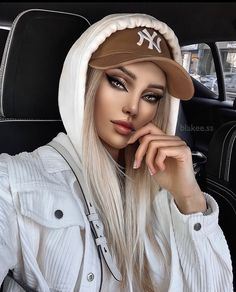 a woman with long blonde hair wearing a baseball cap and white shirt, sitting in the back seat of a car