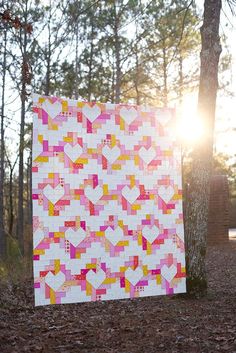 a pink and yellow quilt sitting on top of a forest floor next to a tree