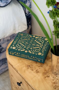 a green book sitting on top of a wooden table next to a flower pot filled with flowers