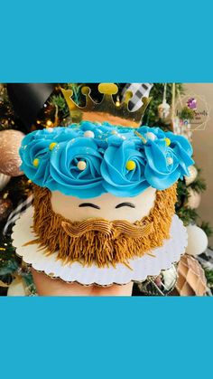 a cake with blue frosting and flowers on it's head sitting in front of a christmas tree